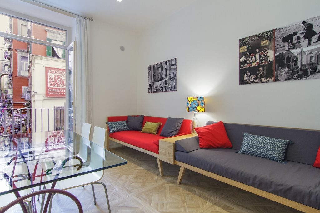 Interior view of Spaccanapoli, Naples, Italy with red sofa with grey cushions, glass dining table and balcony. 