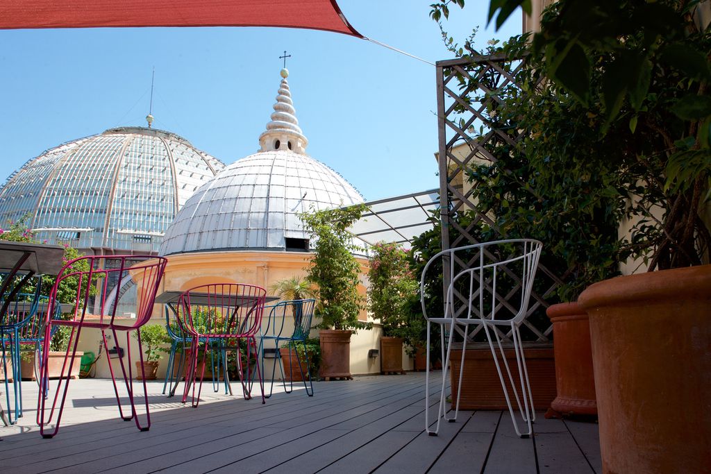 Exterior view, terrace of Attico Partenopeo, Naples Italy. Red and blue chairs, plants and dome.