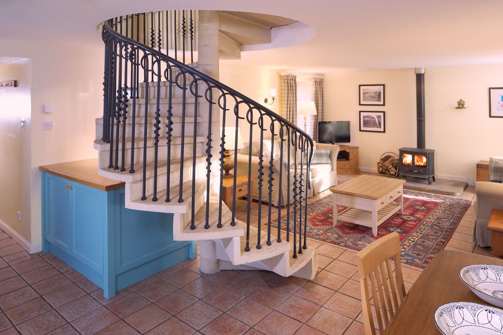 Spacious open plan kitchen, dining and living area with iron spiral staircase leading upstairs and wood burner by the sofas