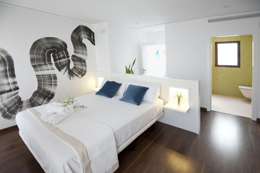 Fresh white bedroom at Mardenit in Alicante, Spain with arty black paint streaks on the wall and an en-suite bathroom
