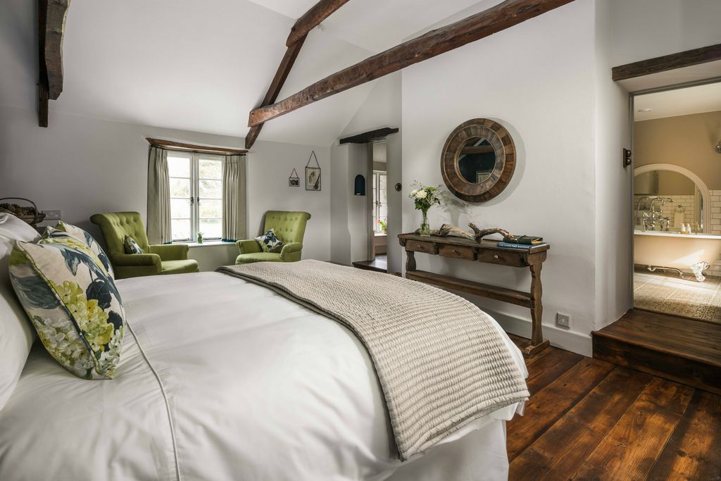 Light and airy bedroom at Hooppells Tor with two armchairs by the window, a lovely wooden table and walkway through to a roll top bath