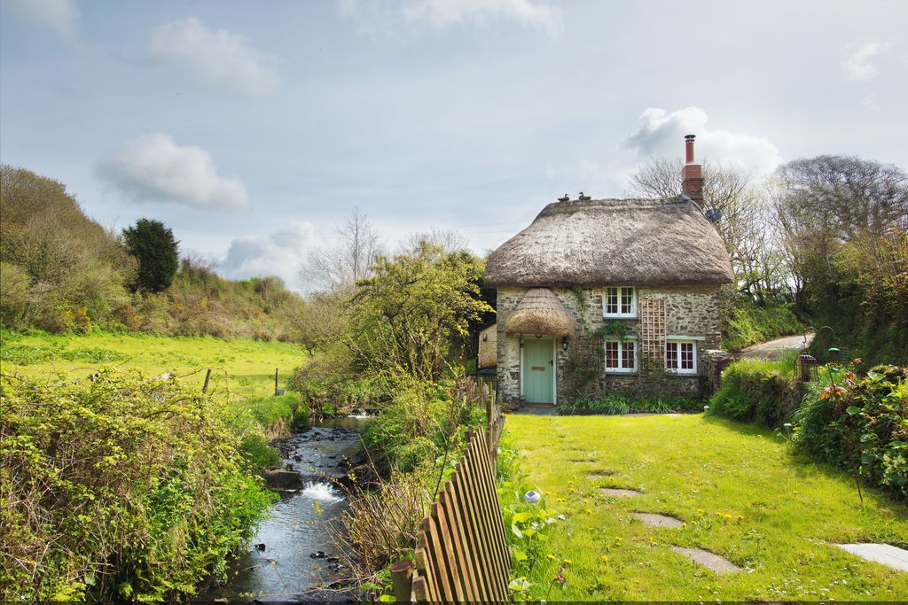 View of thatched-roofed Philham Water Cottage in Bideford, Devon from front garden - a secluded spot with a babbling brook alongside the cottage