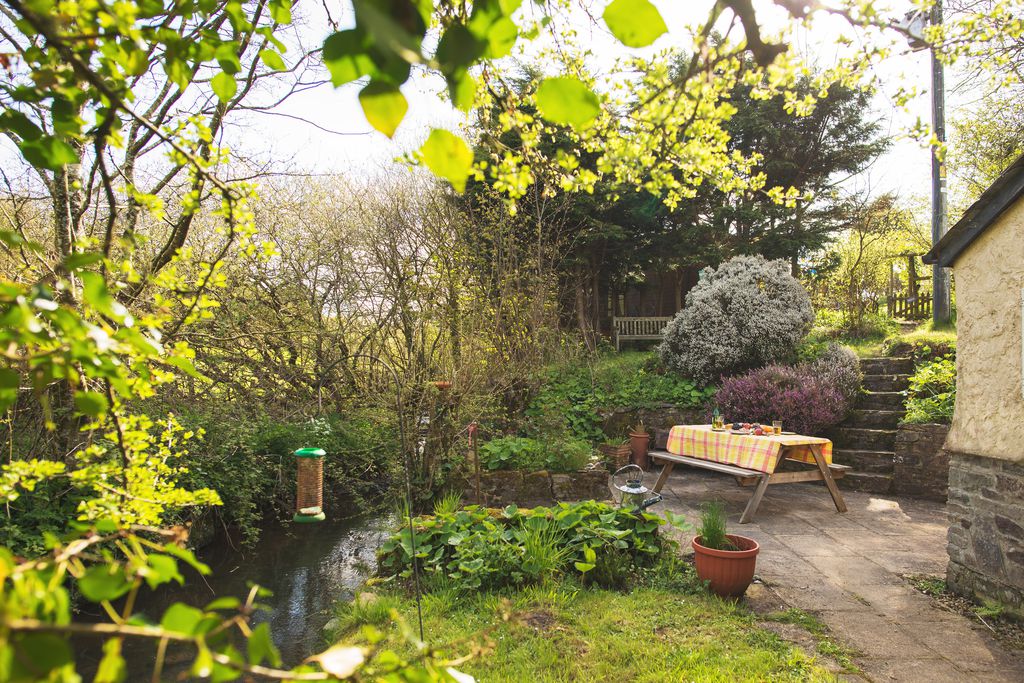 Peaceful spot in the garden at the back of Philham Water Cottage with picnic bench laid for supper, a quiet bench to read a book, and the brook running past