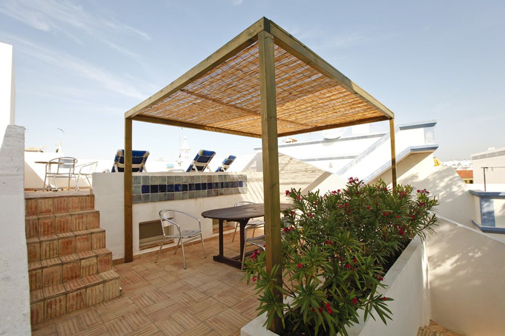 Sunny rooftop terrace at Casa Roberto in Santa Luzia, Algarve, Spain with sun loungers and sheltered seating area for dining