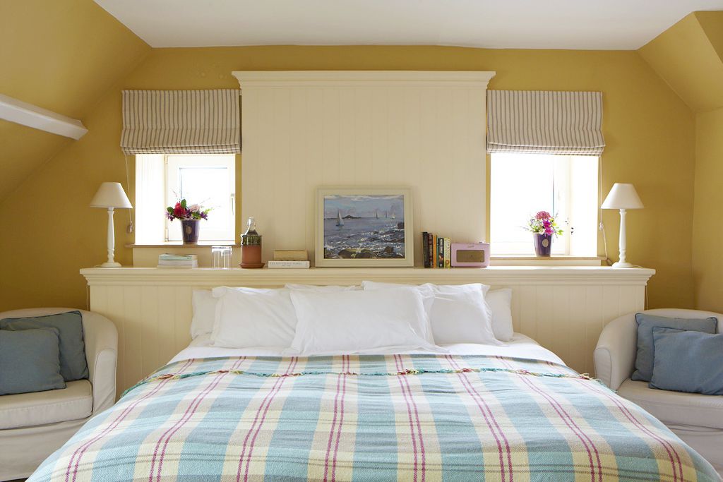 Double bedroom with comfy chairs and a painting of boats on the sea