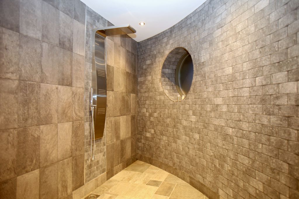 Modern shower with tiled walls and porthole looking out onto the countryside