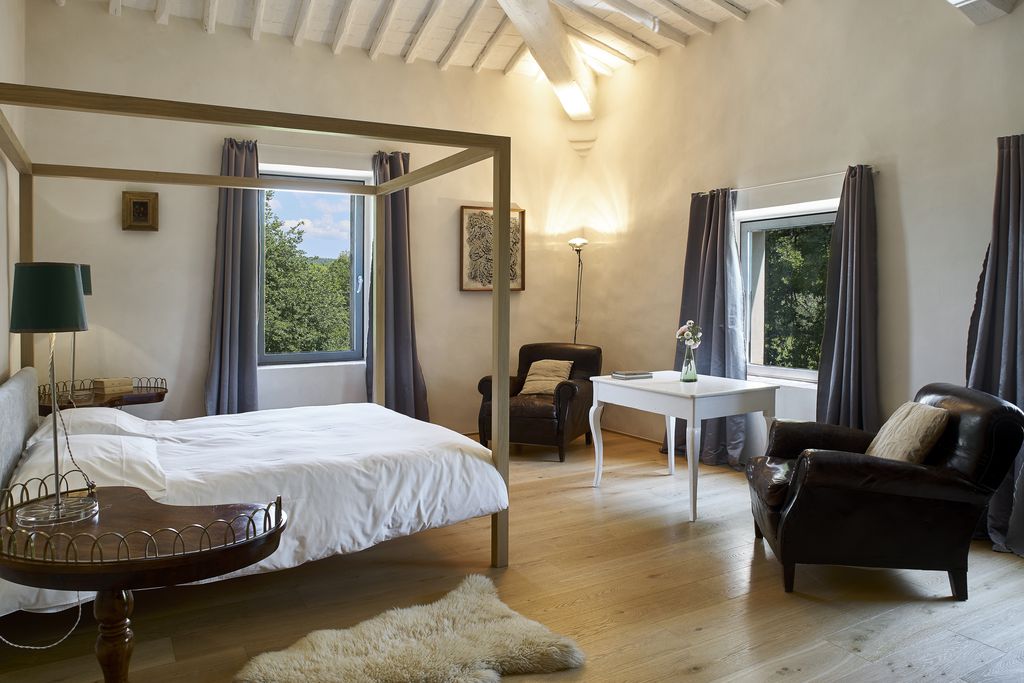 Light and airy bedroom at Casale de Cellole in Tuscany, Italy with four poster bed and two chairs and table with view of countryside