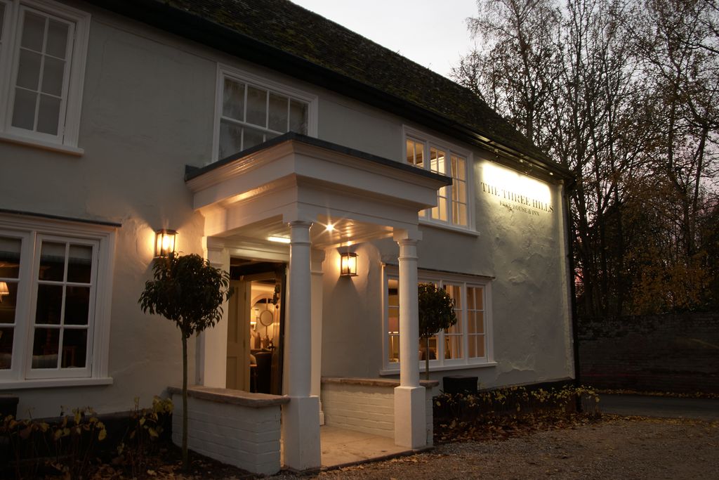 Exterior of The Three Hills pub lit up at dusk in Bartlow, Cambridgeshire