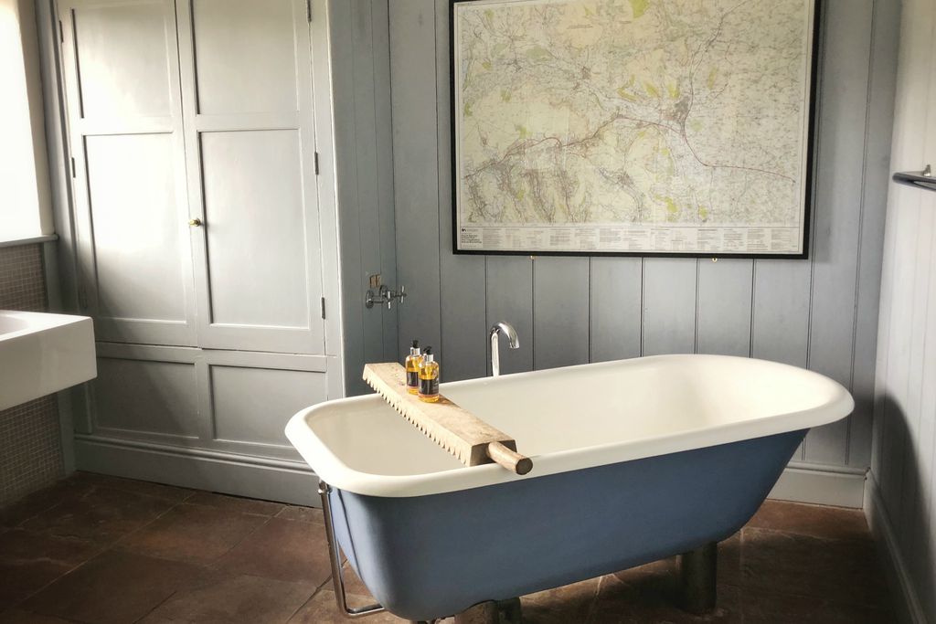 Bathroom at Sycamore House with lovely blue roll top bath against soft grey walls snd OS-style map of local area on the wall