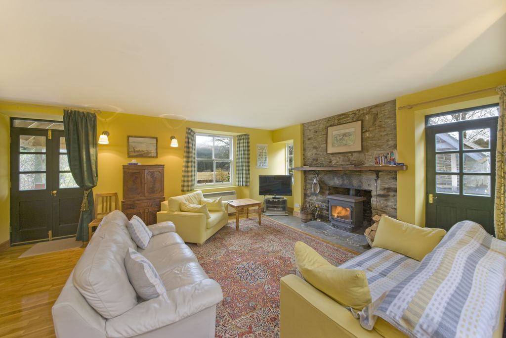 Larger living room with log burner and traditional hearth, with double doors leading on to the grounds