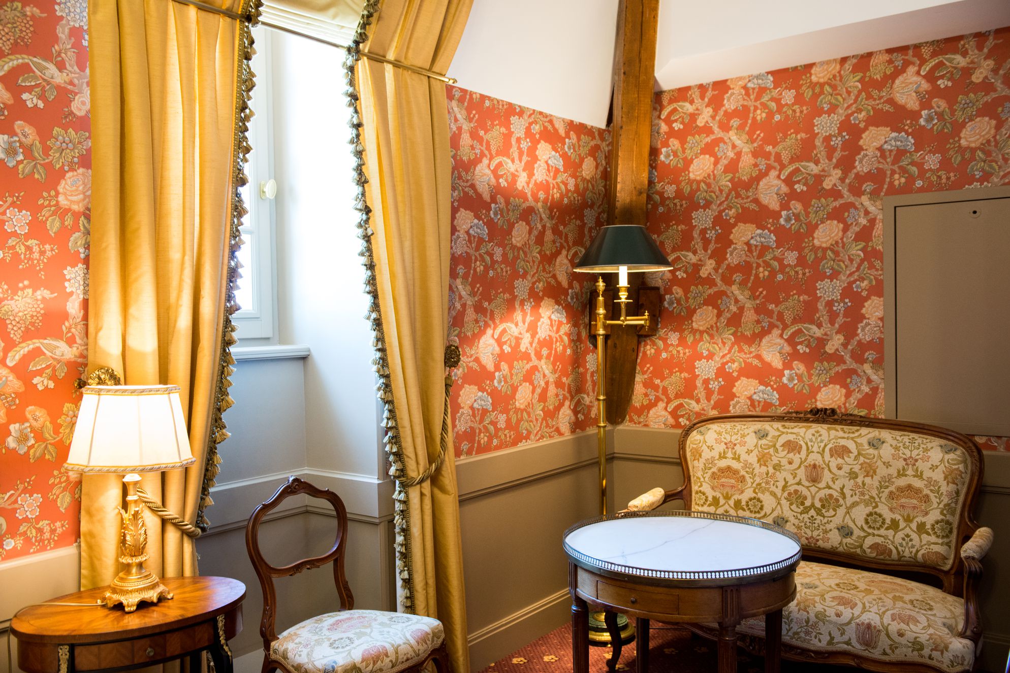 Cosy seating corner at Chateau des Creusettes in La Chapelle du Chatelard in France, with patterned orange wallpaper and gold draped curtains