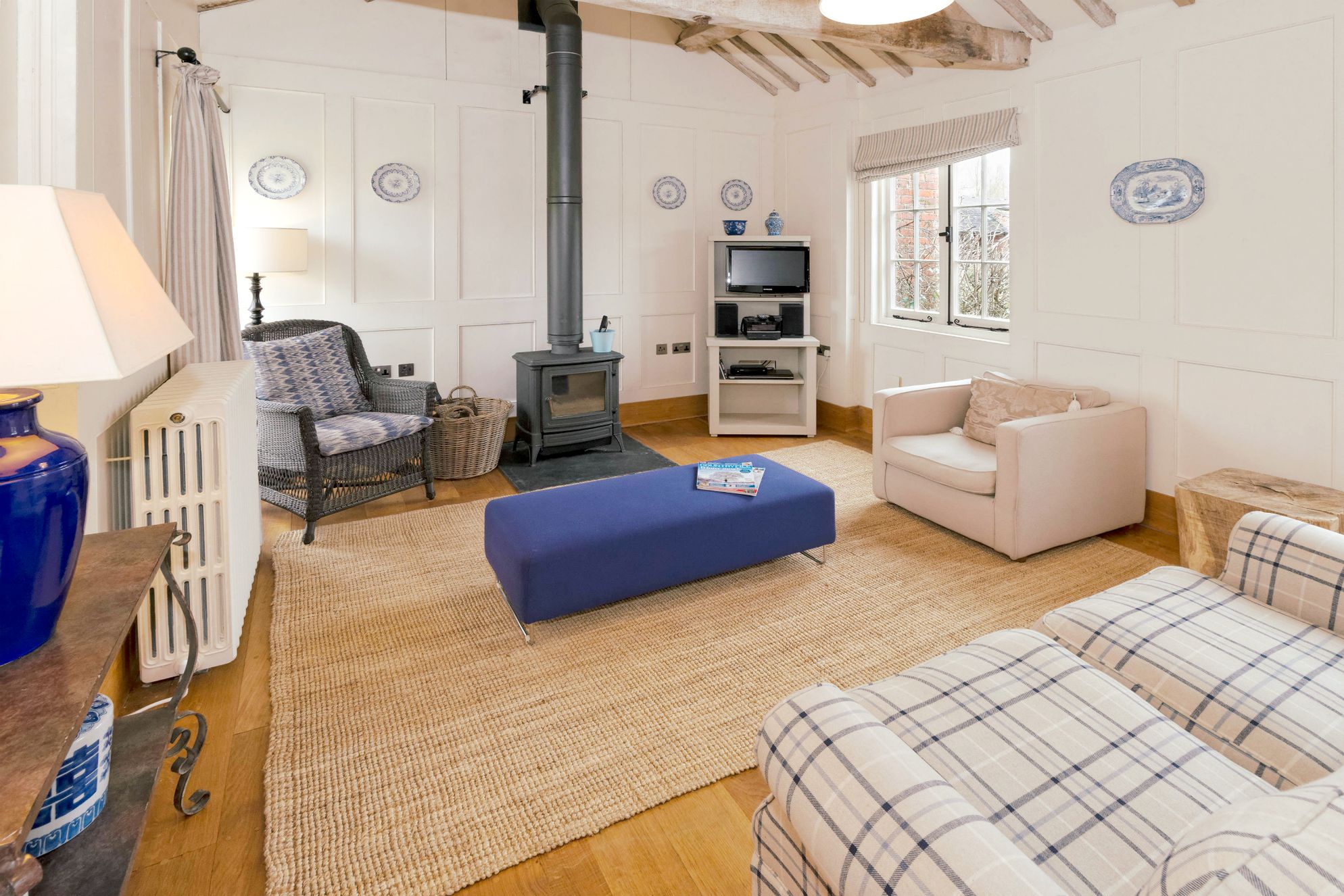 Light and airy living room with white walls and blue tones as well as a wood burner to cosy up in front of on cooler days